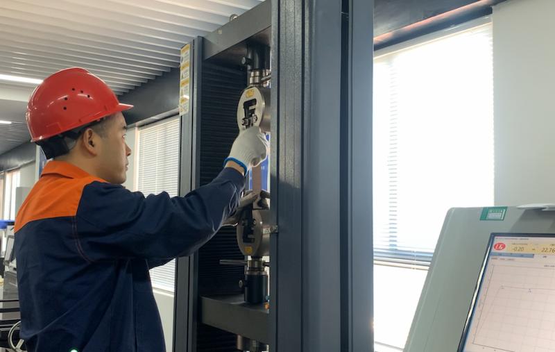Alt Text: Juhong engineer conducting tensile strength and elongation test (>10% high elongation) on steel strapping in ISO certified laboratory.