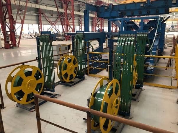 A photograph of a high-speed, fully automated packaging line in operation, utilizing Juhong Packing’s precision-engineered machine-grade PET strapping. The image demonstrates the strap\'s superior dimensional tolerance and consistency, ensuring zero jamming and maximum uptime for continuous 24/7 industrial production. As a cost-effective, rust-free alternative to steel, this PET solution is specifically specifically optimized for robotic friction-welding systems