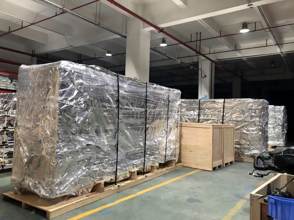 A detailed industrial photograph demonstrating the multi-layer seaworthy packaging process for large heavy machinery. The equipment is first vacuum-sealed in aluminum moisture-barrier foil for anti-corrosion, then overwrapped with protective stretch film, placed inside a heavy-duty wooden export crate, and finally secured externally with Juhong\'s high-tension black steel strapping to ensure structural integrity during global maritime logistics.