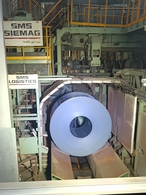 A large steel coil being secured by high-tensile steel strapping from Juhong Packing Materials within a fully automated SMS group (SMS Siemag) heavy industry packaging station.