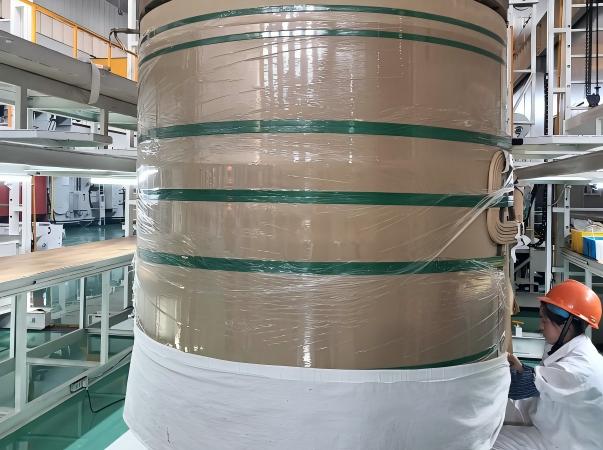 A workshop photograph showcasing Juhong Packing’s integrated protection system for giant industrial paper rolls. The process combines high-performance LLDPE stretch film for a moisture-proof and stain-resistant seal with AAR-certified (ID: 124) PET strapping for heavy-duty structural integrity. As the National Standard Drafter for strapping seals (GB/T 39040—2020), Juhong ensures zero-loss logistics for the world’s largest paper mills during maritime and rail transit.