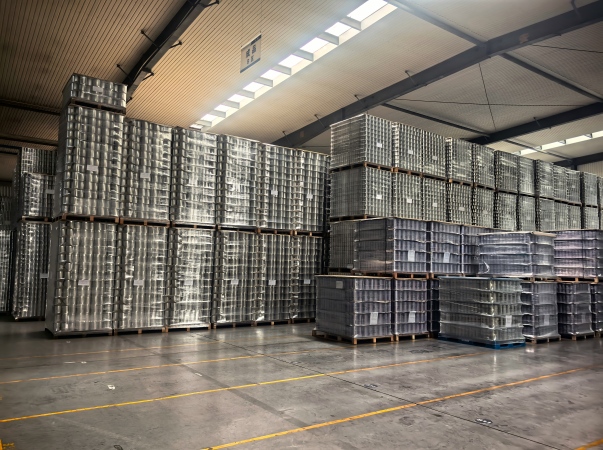 A professional photograph from a canning facility showcasing Juhong Packing’s integrated packaging system for beverage cans. High-performance LLDPE stretch film is used to create a hygienic, dust-proof seal around the pallet, while machine-grade black PET strapping (AAR-certified ID: 124) provides the high-tension vertical stability required for high-speed automation lines. As a National Standard Drafter, Juhong engineered this dual-layer solution