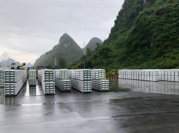 A real-world logistics photograph showing heavy aluminum ingot bundles stored outdoors on continuous wet ground immediately following rain. The ingots are securely bundled with high-tension polyester (PET) strapping. This image demonstrates a critical advantage of Juhong’s PET over traditional steel strapping in metal logistics: complete rust-proof performance, ensuring the high-value aluminum surface remains unstained despite direct exposure to moisture and harsh weather elements.